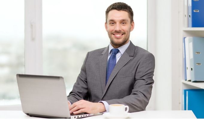 A smiling man in a suit working at his laptop